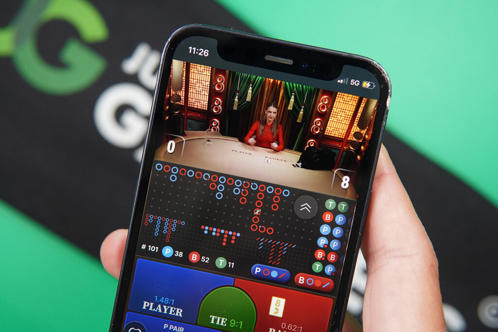 Photo of Patrik Lidin holding an iPhone showing live dealer game Always 8 Baccarat.