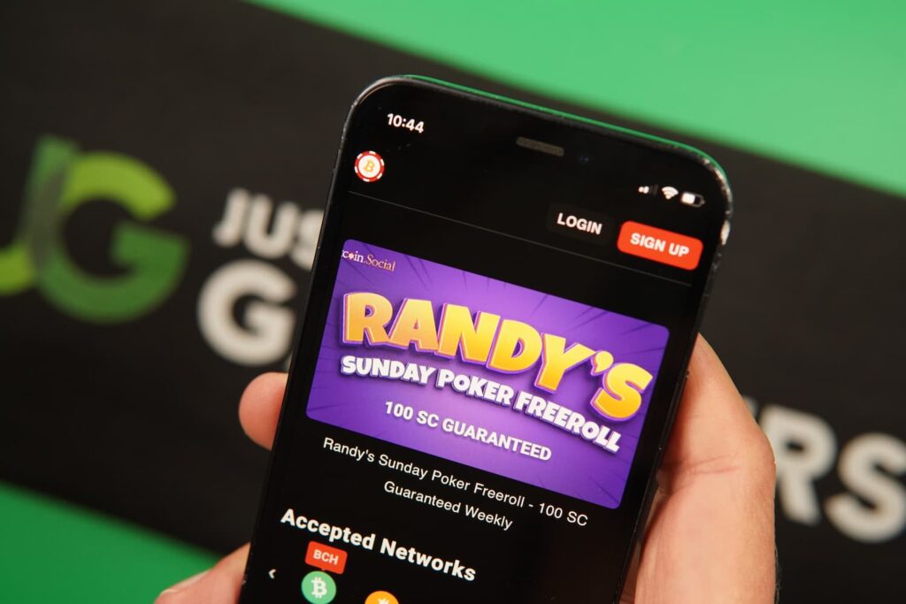 Patrik Lidin holding an iPhone with the BetcoinSocial casino poker freeroll page loaded on the webpage.