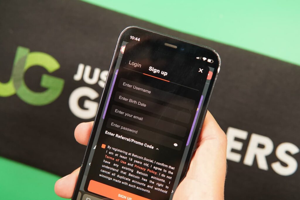 Patrik Lidin holding an iPhone with the BetcoinSocial casino registration page loaded on the webpage.