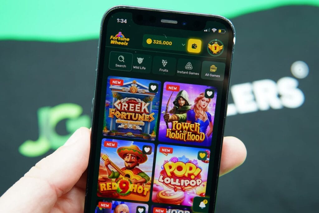 Patrik Lidin holding an iPhone with the Fortune Wheelz casino game library page loaded on the webpage.