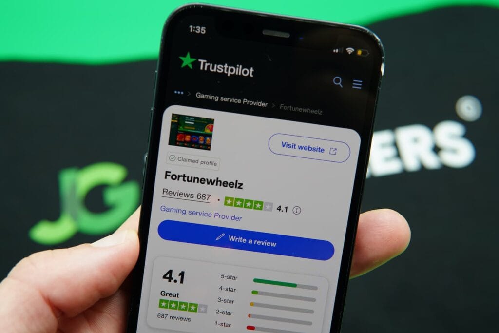 Patrik Lidin holding an iPhone with the Fortune Wheelz casino Trustpilot ratings page loaded on the webpage.
