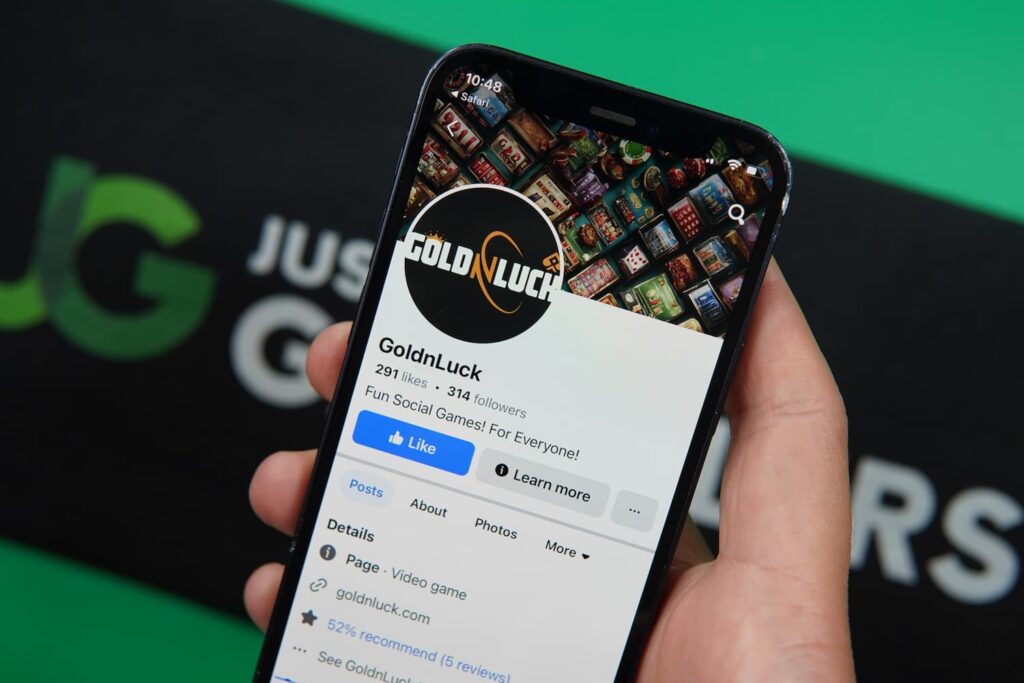 Patrik Lidin holding an iPhone with the GoldNLuck casino social Facebook page loaded on the webpage.