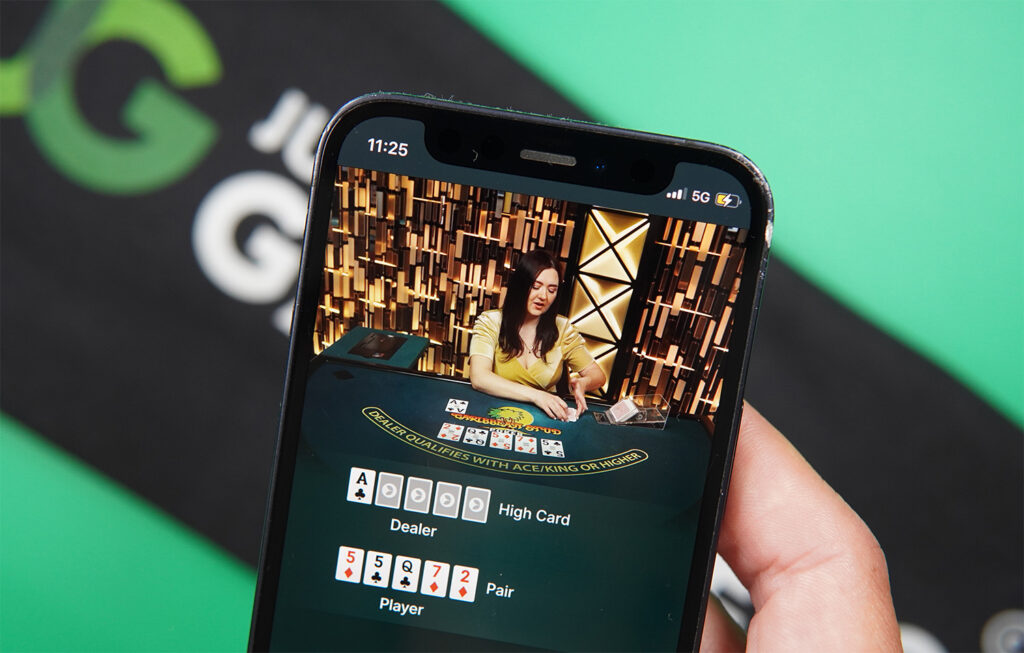 Photo of Patrik Lidin holding an iPhone showing live dealer game Caribbean Stud Poker.