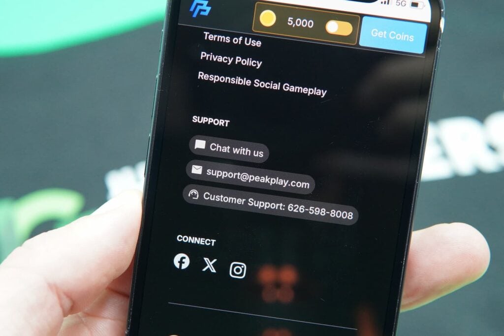 Patrik Lidin holding an iPhone with the PeakPlay casino support page loaded on the webpage.