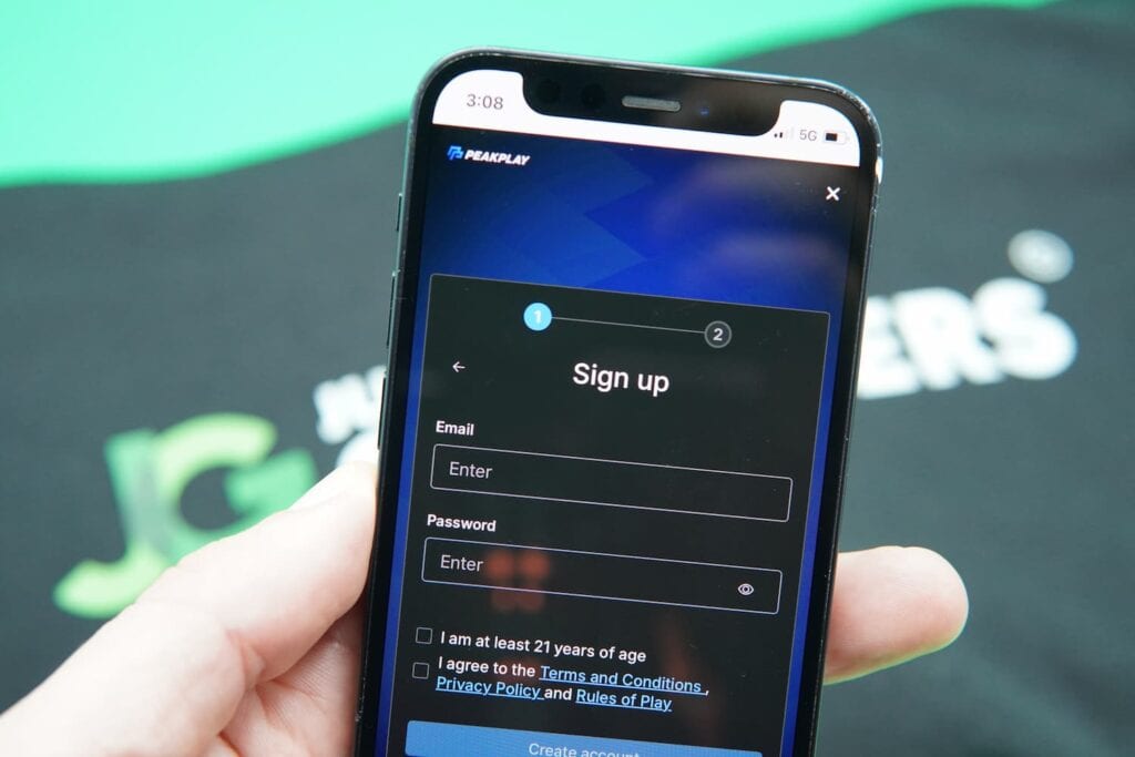 Patrik Lidin holding an iPhone with the PeakPlay casino registration page loaded on the webpage.
