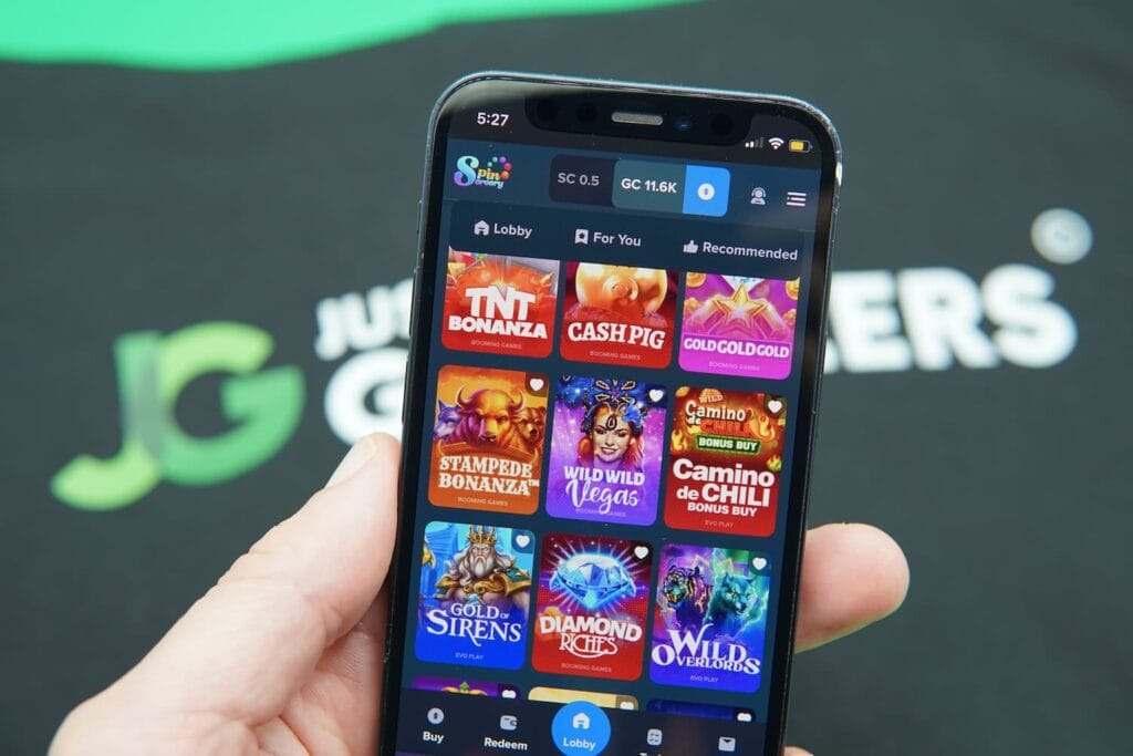 Patrik Lidin holding an iPhone with the Spin Sorcery casino game library page loaded on the webpage.