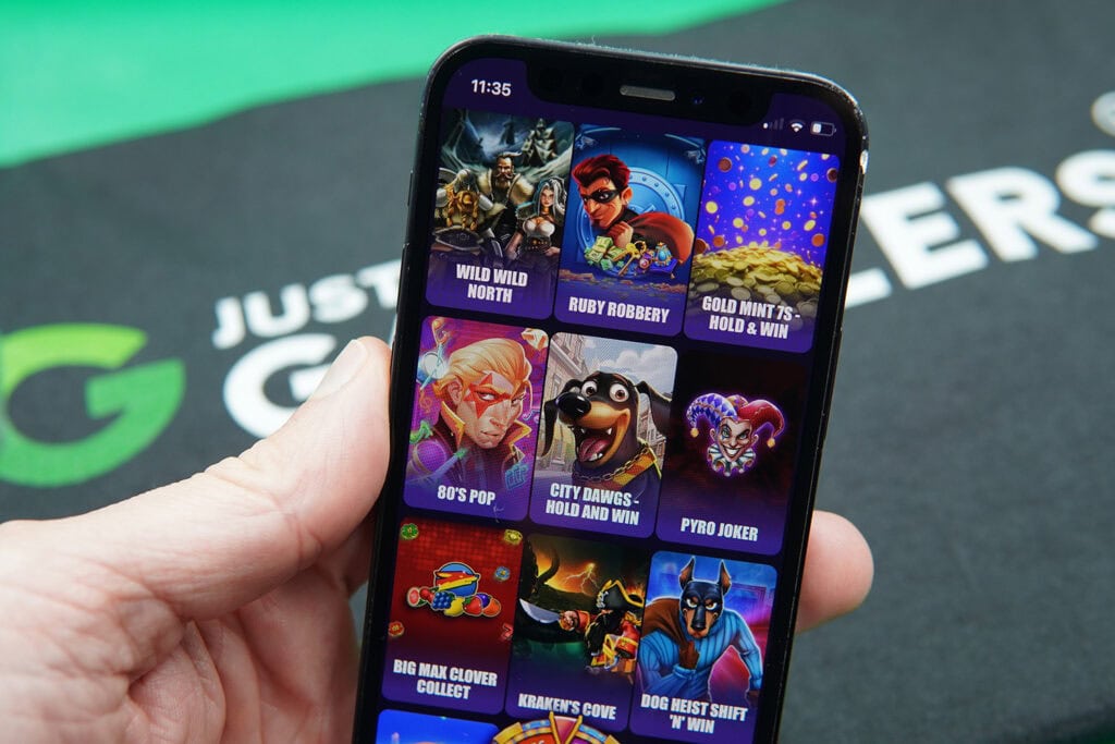 Patrik Lidin holding an iPhone with SweepSlots game library showing.