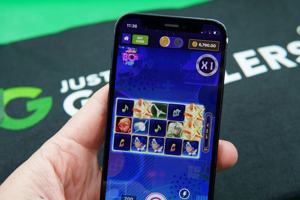 Patrik Lidin holding an iPhone with SweepSlots casino game 80’s Pop showing.