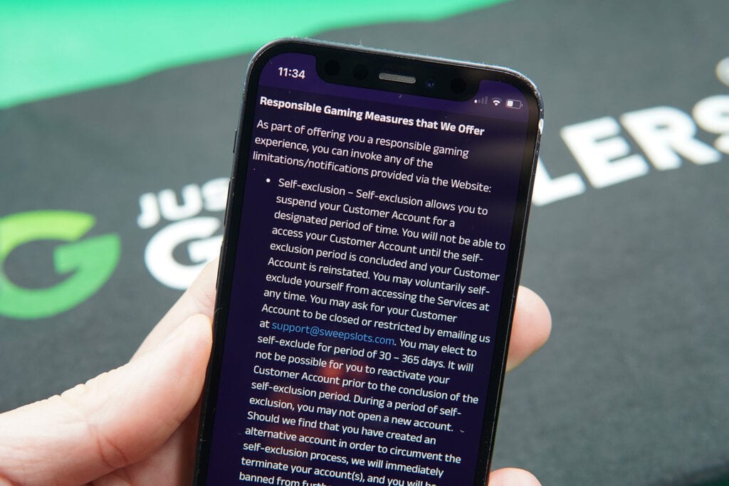 Patrik Lidin holding an iPhone with the SweepSlots responsible gambling page showing.